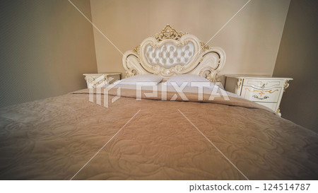 Luxurious beige king size bed with an ornate headboard, pristine white pillows, and matching nightstands, creating a romantic ambiance Luxurious beige king size bed with an ornate headboard, pristine white pillows, and matching nightstands, creating a romantic ambiance 124514787