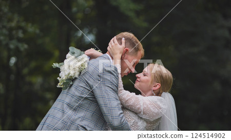 Newlywed couple sharing a tender moment, embracing in a wooded area, with the bride holding a bouquet 124514902