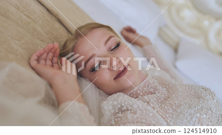 Elegant bride relaxing on bed, wearing white wedding gown with pearl accents, soft veil draping, capturing serene wedding morning moment Elegant bride relaxing on bed, wearing white wedding gown with pearl accents, soft veil draping, capturing serene wedding morning moment 124514910