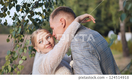 Newlywed couple sharing a tender moment under a birch tree, celebrating their wedding day with love and happiness Newlywed couple sharing a tender moment under a birch tree, celebrating their wedding day with love and happiness 124514918