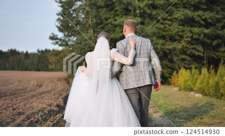 Newlyweds strolling hand in hand along woodland path, sharing intimate moment after wedding ceremony 124514930