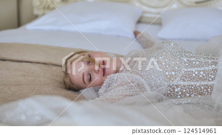 Bride wearing white wedding dress relaxing on soft bed, capturing peaceful moments before walking down aisle Bride wearing white wedding dress relaxing on soft bed, capturing peaceful moments before walking down aisle 124514961