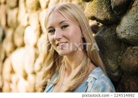 Blonde teenager smiling, wearing hoop earrings, leaning against stone wall backdrop Blonde teenager smiling, wearing hoop earrings, leaning against stone wall backdrop 124514992