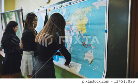 Teenage girls in geography class hanging a world map on the blackboard and discovering countries and continents Teenage girls in geography class hanging a world map on the blackboard and discovering countries and continents 124515059
