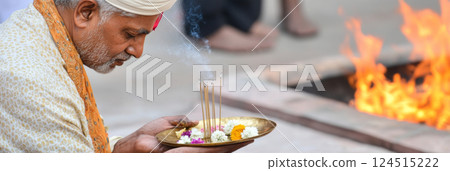 Indian man with tray of flowers and incense by fire during Holika Dahan Indian man with tray of flowers and incense by fire during Holika Dahan 124515222