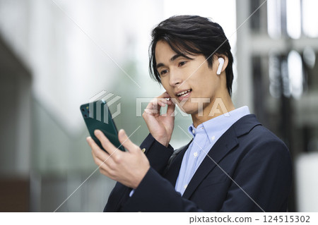 一名 20 多歲的男子戴著耳機，手裡拿著智慧型手機 124515302