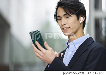 一名 30 多歲的男子戴著耳機看著智慧型手機螢幕 一名 30 多歲的男子戴著耳機看著智慧型手機螢幕 124515479