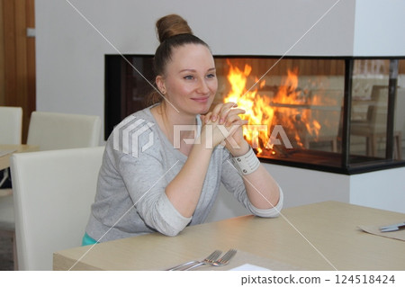 Young girl sitting at table looking out window next to fireplace 124518424