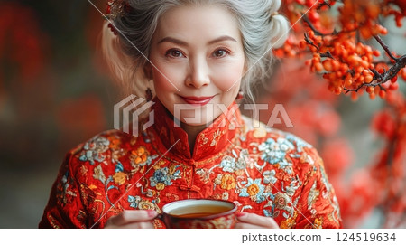A graceful elderly woman in a vibrant red Chinese embroidered outfit holds a teacup, radiating warmth and joy, surrounded by lush red berries, symbolizing prosperity and harmony for Chinese New Year. A graceful elderly woman in a vibrant red Chinese embroidered outfit holds a teacup, radiating warmth and joy, surrounded by lush red berries, symbolizing prosperity and harmony for Chinese New Year. 124519634