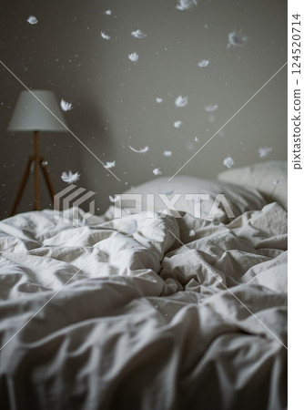 Feathers gently falling over neatly spread bed linens in soft, cozy bedroom atmosphere of comfort 124520714
