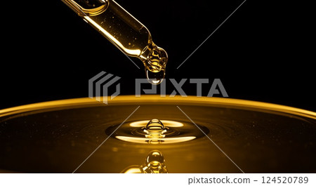 Golden pipette with a falling drop of oil in warm light 124520789