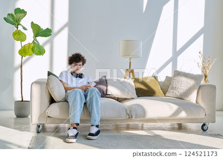Young guy 20 years old sitting at home on the couch using smartphone Young guy 20 years old sitting at home on the couch using smartphone 124521173