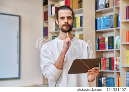 Young handsome man with digital tablet looking at camera inside library office Young handsome man with digital tablet looking at camera inside library office 124521407