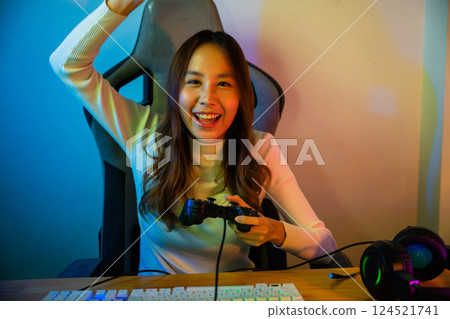 Winning. Happy Gamer using joystick controller for virtual tournament plays online video game with computer she raises hands to wins celebrating, Asian woman wearing gaming headphones feeling excited 124521741