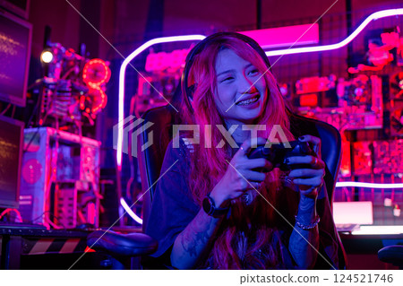 Gamer using joystick controller for virtual tournament plays online video game with computer neon lights dark room, woman wear gaming headphones playing live stream esports games console at home 124521746