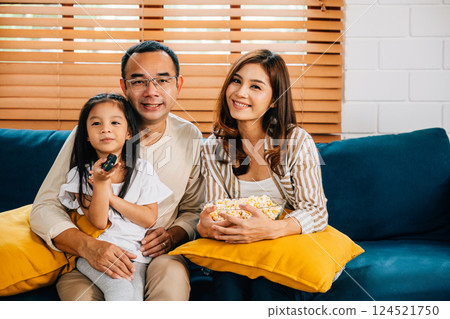 Family time is fun and relaxation as the family watches a movie in the living room with popcorn. The father mother son daughter and schoolgirl are all smiles bonding in happiness. 124521750