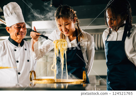 Chef trains in kitchen. Schoolgirls cook Japanese noodle. Kids and teacher at stove. Smiling portrait of learning is modern education. Making dinner with ladle gives joy. Foor Education Concept 124521765