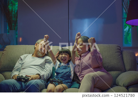 Happy Asian family bonding over a video game on a cozy couch, little girl winning after playing video games console with senior grandparents by controller joysticks while sitting on the sofa Happy Asian family bonding over a video game on a cozy couch, little girl winning after playing video games console with senior grandparents by controller joysticks while sitting on the sofa 124521780