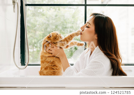 Capturing a serene moment, an attractive adult woman enjoys her bath in the bathroom, sharing precious pet love with her Scottish Fold cat. Capturing a serene moment, an attractive adult woman enjoys her bath in the bathroom, sharing precious pet love with her Scottish Fold cat. 124521785