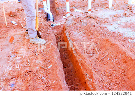 Worker uses shovel to dig trench in dry soil for plumbing installation at construction site 124522941