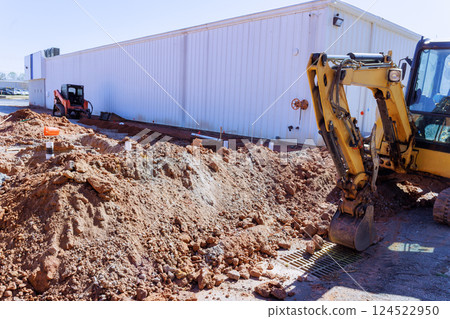 Excavation is underway with heavy machinery near commercial building, surrounded by dirt, materials. Excavation is underway with heavy machinery near commercial building, surrounded by dirt, materials. 124522950