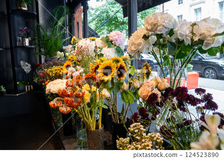 Colorful flowers in vases and bouquets are arranged neatly inside a florist shop. The natural light and variety of blooms create a fresh, elegant atmosphere. 124523890