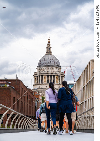 The view of St. Pauls Cathedral from Millennium Bridge is vibrant, with people strolling toward it, blending modern movement with historic architecture. 124523908