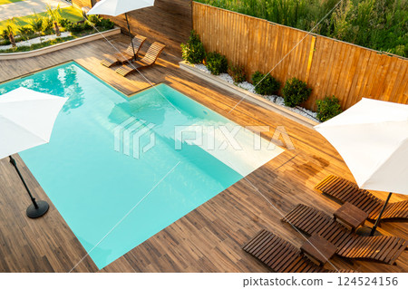 Modern turquoise swimming pool with wooden deck, lounge chairs, and umbrellas in a stylish backyard Modern turquoise swimming pool with wooden deck, lounge chairs, and umbrellas in a stylish backyard 124524156