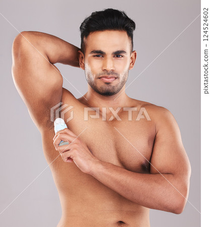 Deodorant, health and man cleaning armpit against a grey studio background. Wellness, care and portrait of a young model with an underarm product for grooming, clean skin and care for body hygiene 124524602