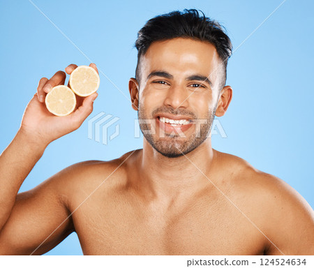 Face, skincare and orange with a man model in studio on a blue background to promote natural beauty. Portrait, fruit and wellness with a handsome young male posing for a health product or treatment 124524634