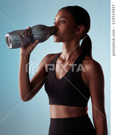Fitness woman drinking water bottle in studio, training and workout, exercise or sports challenge on blue background. Thirsty young athlete, hydration rest or wellness, healthy lifestyle or nutrition 124524947