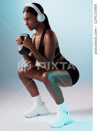 Woman, kettle bell or headphones in training on studio background for exercise, workout or health. Personal trainer, fitness model or sports person squatting with weights, music or motivation podcast Woman, kettle bell or headphones in training on studio background for exercise, workout or health. Personal trainer, fitness model or sports person squatting with weights, music or motivation podcast 124525069