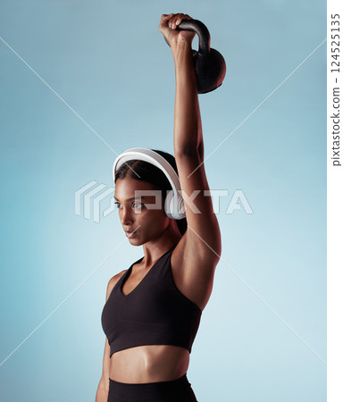 Fitness, music and woman lifting a kettlebell in studio strength training, sports workout and full body exercise. Healthy, sports and Indian girl with strong arms streaming a podcast audio or radio 124525135