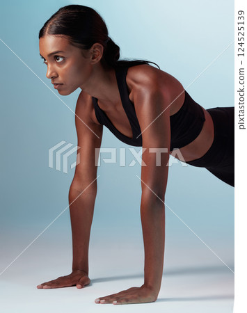 Fitness, exercise and focus with a sports woman in studio on a blue background doing pushups for strong muscles. Training, health and workout with a young female athlete exercising for wellness 124525139