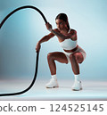 Woman, battle rope and exercise on blue background in studio resistance training, energy sports or cardio workout. Personal trainer, fitness model or person with wellness health goals for arm muscles 124525145