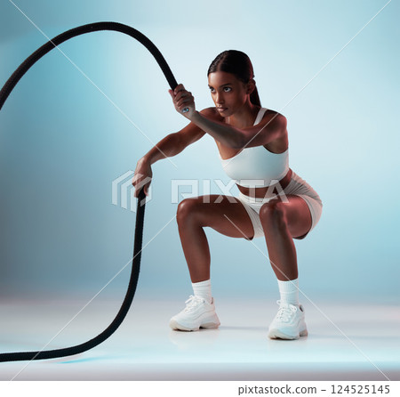 Woman, battle rope and exercise on blue background in studio resistance training, energy sports or cardio workout. Personal trainer, fitness model or person with wellness health goals for arm muscles 124525145