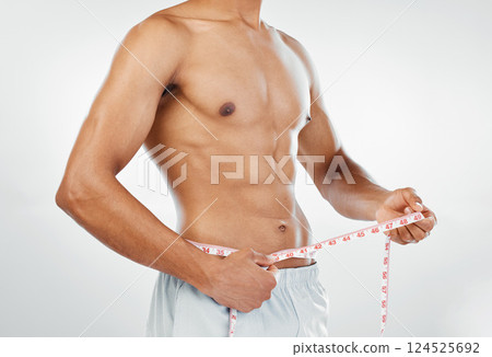 Man, measuring tape with weightloss and diet, body wellness and healthy lifestyle, weight check with bare abdomen. Fitness, health and muscle, shirtless and abs with fat or slim in studio background. Man, measuring tape with weightloss and diet, body wellness and healthy lifestyle, weight check with bare abdomen. Fitness, health and muscle, shirtless and abs with fat or slim in studio background. 124525692