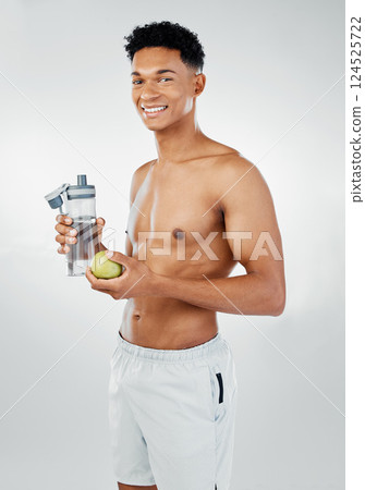 Fitness, apple and man drinking water in studio after training, cardio workout and exercise for body wellness. Lifestyle, fruit and healthy young athlete or happy personal trainer on a vegan diet 124525722