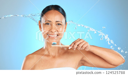 Dental, health and woman brushing teeth with toothbrush, toothpaste and water splash on blue studio background. Healthcare, self care product and oral care hygiene of mature Brazilian beauty model. Dental, health and woman brushing teeth with toothbrush, toothpaste and water splash on blue studio background. Healthcare, self care product and oral care hygiene of mature Brazilian beauty model. 124525788