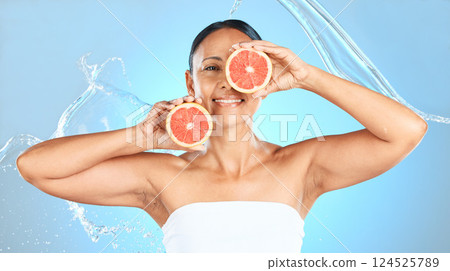 Beauty, cleaning and grapefruit by woman in studio for health, wellness and cosmetic treatment against blue background. Fruit, skin and model relax with detox, diet and water skincare splash product 124525789