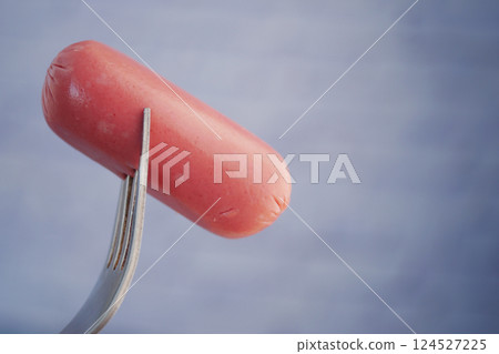 Fork holding a hot dog against a light background in kitchen setting Fork holding a hot dog against a light background in kitchen setting 124527225