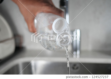 Pouring clear water from a plastic bottle into a kitchen sink Pouring clear water from a plastic bottle into a kitchen sink 124527237