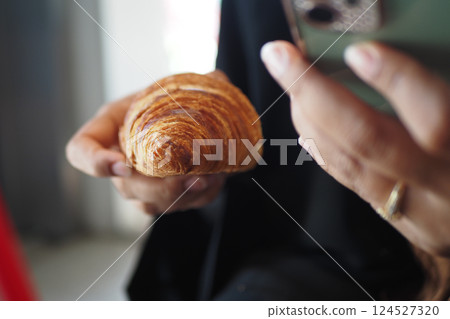 Delicious croissant held in hand while using a smartphone 124527320