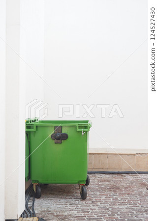 Green trash bin positioned in a corner of a clean outdoor area 124527430