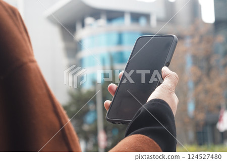 Person holding a smartphone in an urban environment during daylight 124527480