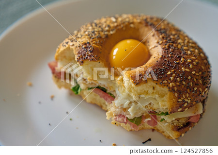 Half-eaten bagel sandwich with egg yolk, cheese and ham on plate 124527856
