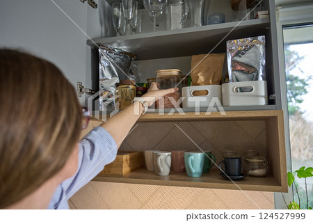 Woman reaching for jar in kitchen cabinet with stored cooking ingredients Woman reaching for jar in kitchen cabinet with stored cooking ingredients 124527999