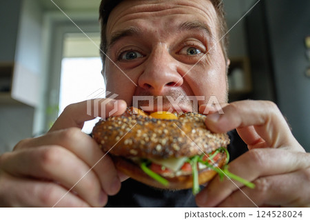 Close-up of hungry man eating breakfast sandwich, biting bagel with egg 124528024