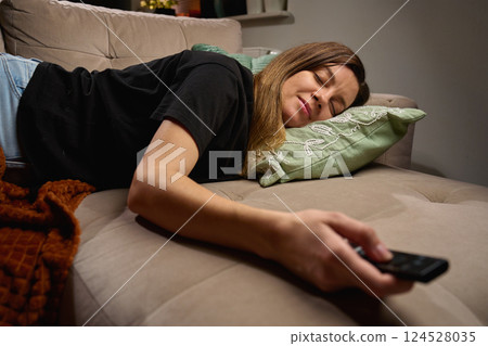 Tired woman relaxing on couch with TV remote, Watching TV 124528035