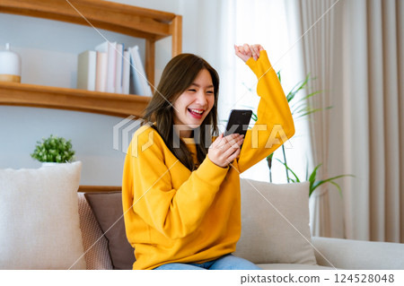 Happy young asian woman relax on comfortable couch at home texting messaging on smartphone Happy young asian woman relax on comfortable couch at home texting messaging on smartphone 124528048